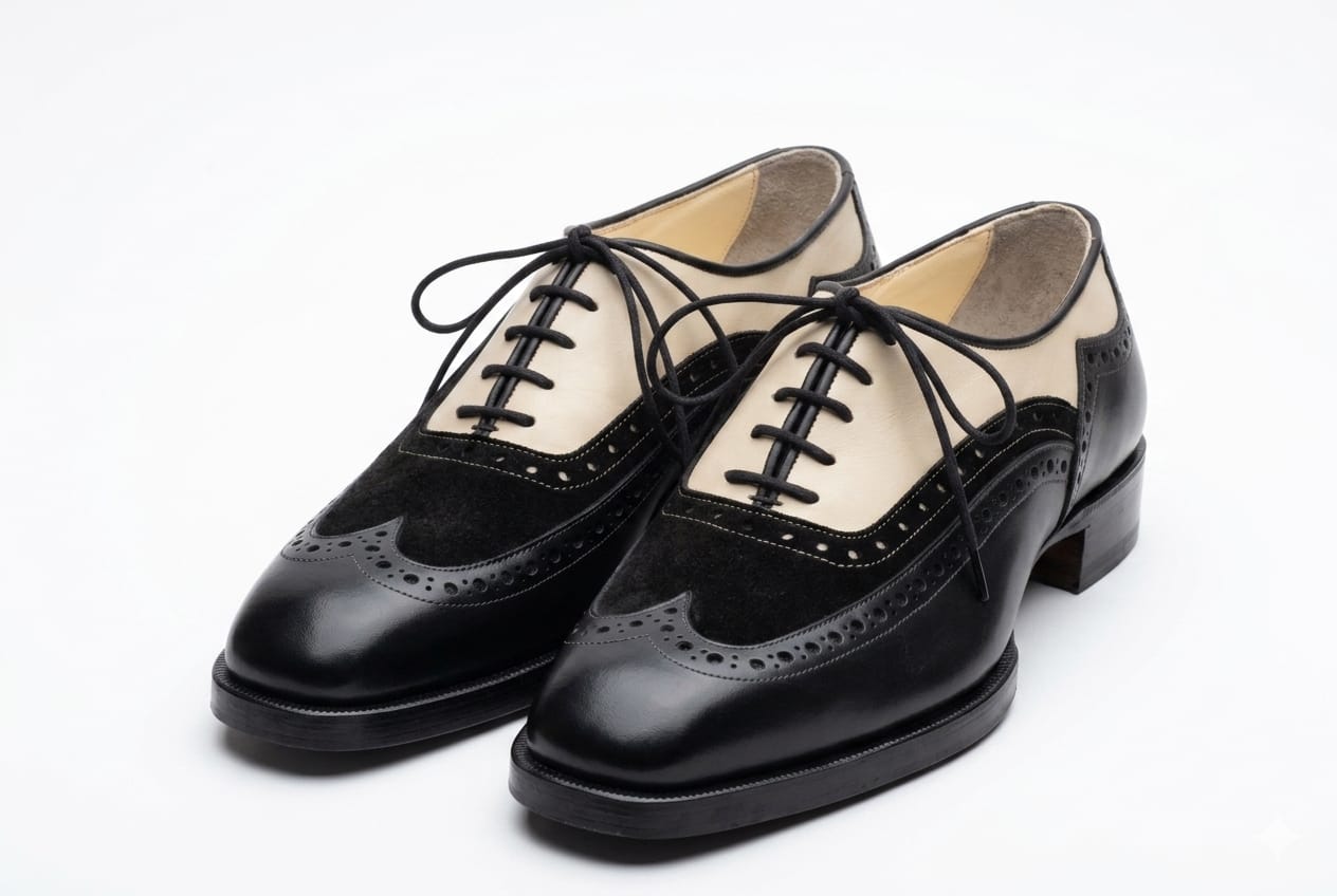 Black leather shoe with brogue details held by a hand on a white background